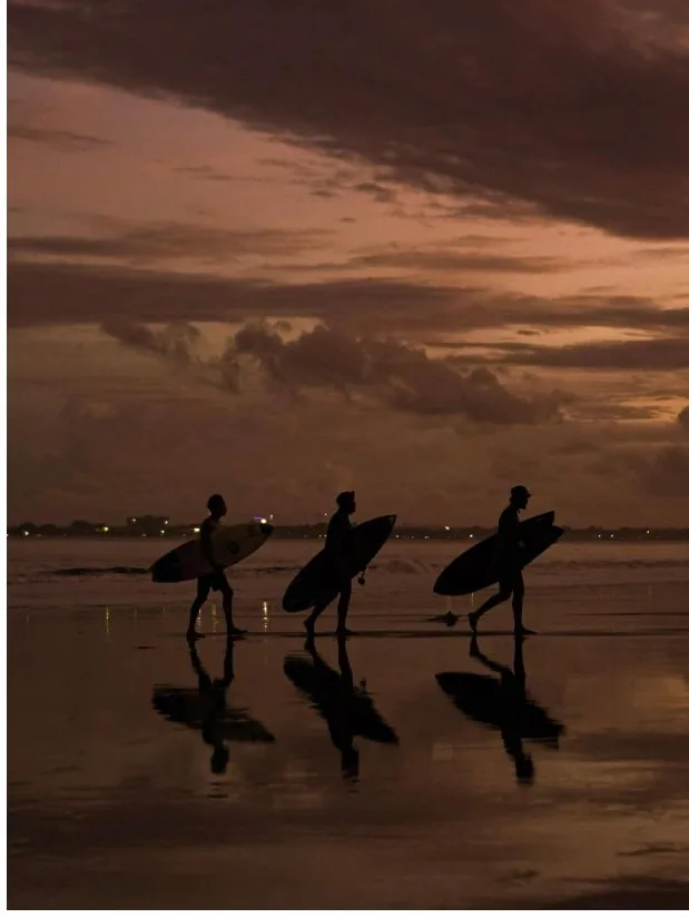 Three surfers silhouetted against a sunset on the beach.