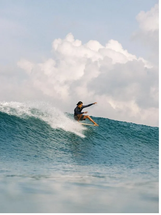 Surfer riding a blue wave beneath a bright sky.